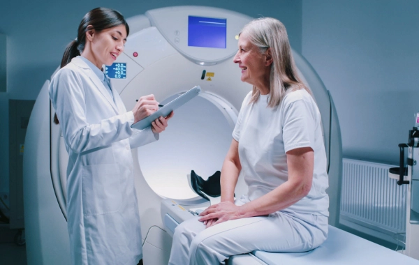 A female doctor consulting with a female patient beside an MRI machine in a radiation therapy examination room.